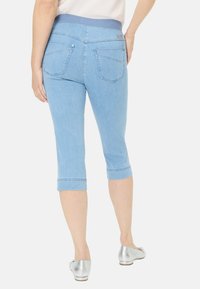 Helle blaue Caprihosen mit einem weichen Bund, Denim-Optik und zwei Gesäßtaschen. Aufgerollte Säume und silberne Akzente an den Schuhen.