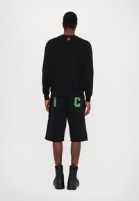 Svart hettegenser med rødt logo på baksiden, kombinert med svarte shorts med grønne bokstaver "I" og "C" på baklommene. Svart støvler.