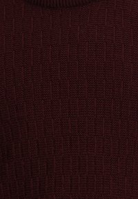 Maglione bordeaux lavorato a maglia con motivo testurizzato a righe in rilievo, collo tondo e bordo a coste al colletto.