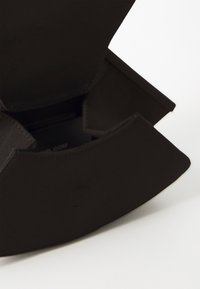 Čierna kabelka na clutch s hladkým, matným povrchom, vybavená zakriveným zavieraním a jemným logom na prednej strane.