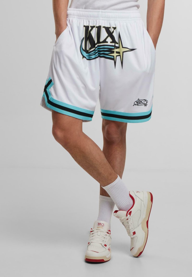 Weiße Sportshorts mit schwarzen und türkisfarbenen Akzenten, die mit einem auffälligen "KIX"-Grafikdesign und einem Sternenmuster versehen sind. Sie verfügen über einen elastischen Bund und seitliche Taschen.