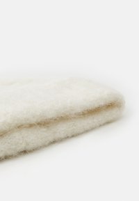 Tessuto in lana color crema piegato, con una superficie morbida e pelosa, caratterizzato da una tonalità uniforme e chiara, priva di motivi o accenti visibili.