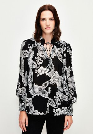 Black blouse with white paisley and floral pattern, featuring a high neckline with a tie, smocked shoulders, and long puff sleeves.