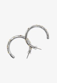 Sølv hoop øreringer med en polert finish, som har små gyldne detaljer og et teksturert, bølgete design. Bakgrunns lukking.