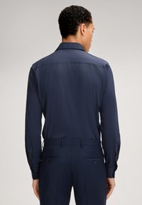 Marineblauwe langesleeve shirt met een gladde textuur en een getailleerde pasvorm. Beschikt over knoopmanchetten en een rugpaneel, gecombineerd met bijpassende broeken.