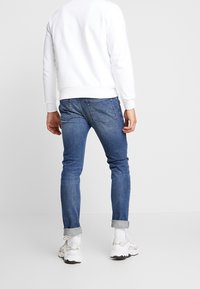 Modré denimové džíny se Slim fit, s ohrnutými nohavicemi. Spárované s bílou mikinou a šedobílými teniskami.