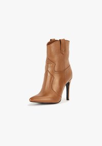 Botte montante en cuir marron jusqu'au milieu du mollet, à talon haut avec bout pointu et couture décorative, présentée sur un fond blanc.