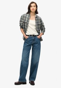 Rutet flannel skjorte i grå og blå, hvid tank top, højhalsede blå jeans og burgunder loafers med et tykt sort bælte.