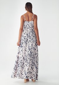 Robe maxi en tissu léger avec une base blanche et un motif à pois bleu marine. Dispose de fines bretelles et d'un design taille cintrée.