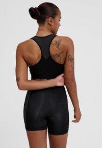 Svart atletisk crop top med meshbakdel, matchad med högmidjade svarta shorts. Slät textur, figurnära design och kontrasterande ribbade accenter.