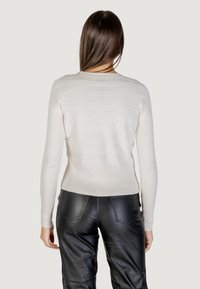 Maglione lungo beige chiaro a maniche lunghe con texture a coste orizzontali e design aderente. Abbinato a pantaloni in pelle nera.