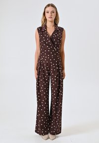 Bruine jumpsuit met stippen, voorzien van een V-hals, mouwloos ontwerp en wijde broekspijpen. Heeft een getailleerde taille en een zachte stoftextuur.