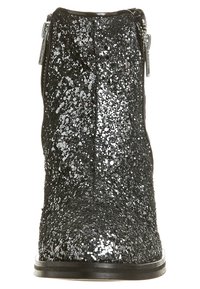 Bottine noire couverte de paillettes argentées, avec un design épuré, un bout rond et une fermeture éclair sur le côté pour un enfilage facile. Semelle noire en dessous.