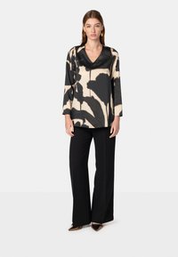 Top a maniche lunghe con scollo a V caratterizzato da un motivo astratto di foglie nere e beige, abbinato a pantaloni larghi neri e scarpe con punta.