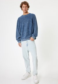 Sudadera de algodón azul con un ajuste relajado, cuello y puños acanalados, combinada con jeans de denim claro y zapatillas blancas.