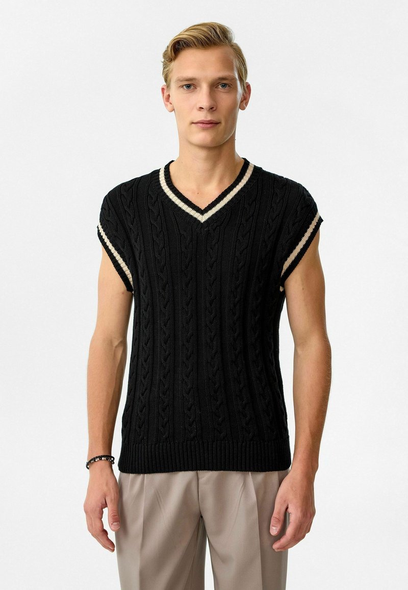 Zwart gebreid sweater met korte mouwen en een V-hals, voorzien van een kabelpatroon en lichtgekleurde geribbelde accenten op de halslijn en mouwen.