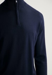 Maglione in maglia blu navy con colletto alto e chiusura a mezza zip. Texture morbida, design slim-fit e maniche lunghe. Stile pulito e minimalista.