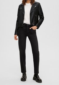 Schwarze Lederbikerjacke mit Reißverschlusstaschen über einem weißen T-Shirt, kombiniert mit schwarzen geraden Jeans und schwarzen klobigen Stiefeln.