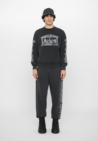 Sort bomulds sweatshirt med "Aries" tryk, matchende tætsiddende bukser og en logo-kasket. Alle dele har en struktureret finish og en afslappet pasform.