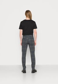 Czarna koszulka i szare spodnie w kratkę z niebieskimi i czarnymi akcentami, slim fit, cztery kieszenie oraz gładka tekstura. Czarne botki do kostek dopełniają stylizację.