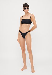 Melna bikini komplekts ar minimālu segumu; bandeau tops ar plānām siksniņām un augstas griezuma apakšdaļām, gluda tekstūra, bez rakstiem un elegants dizains.