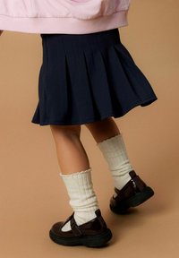 Gonna plissettata blu navy abbinata a calze a costine crema e scarpe T-strap marrone scuro. L'outfit presenta una vestibilità comoda e tessuti morbidi.