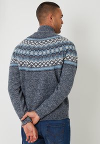 Maglione lavorato a maglia di colore blu scuro con colletto alto. La parte superiore presenta un motivo geometrico in blu chiaro e bianco. Tessuto morbido, maniche lunghe.