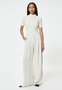 Top de punto de canalé crema con mangas cortas combinado con pantalones de crema de talle alto y pierna ancha. Zapatos negros de punta afilada completan el look.