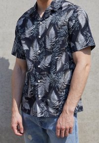 Korte mouwen shirt met een donker marineblauwe achtergrond en ingewikkelde groene en witte varenpatronen, gemaakt van lichtgewicht stof met knoopsluitingen.