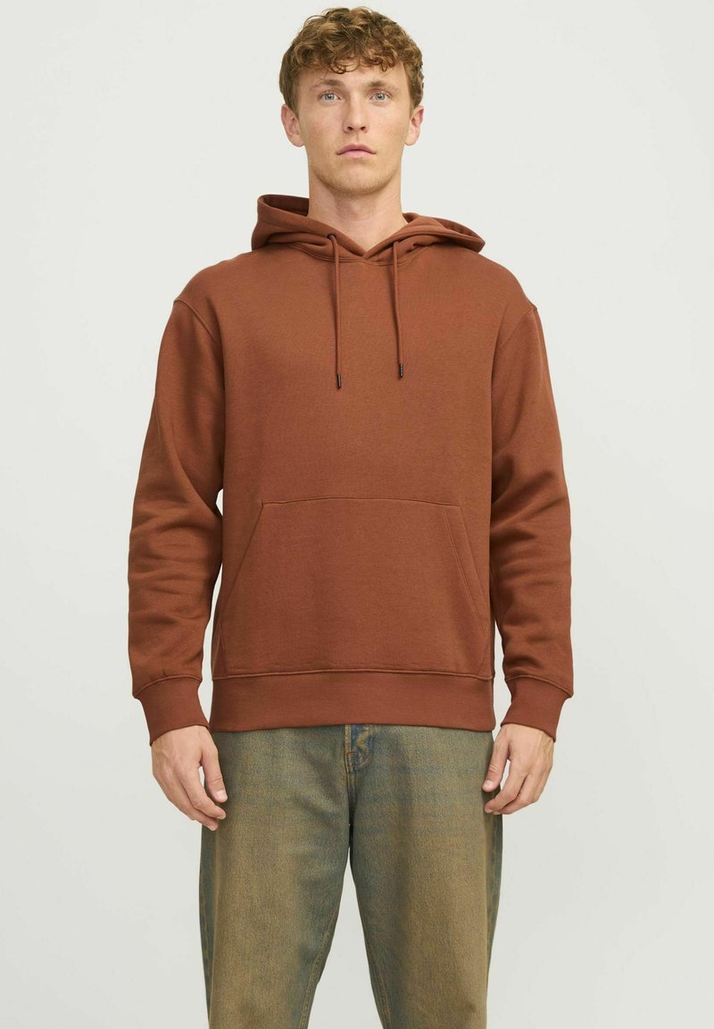 Brown hooded sweatshirt made of a smooth fabric, featuring a front pocket, drawstrings, and ribbed cuffs, paired with light jeans.