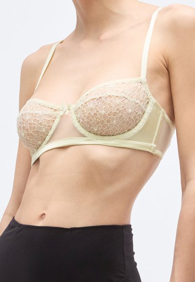 Sujetador de encaje amarillo claro con copas transparentes y banda de satén, con tirantes ajustables y un pequeño detalle de lazo en el centro.