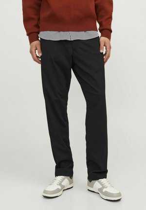 Pantaloni neri leggeri con vestibilità dritta, indossati con un maglione rosso a maglia e una camicia a righe sotto, abbinati a sneakers bianche e grigie.