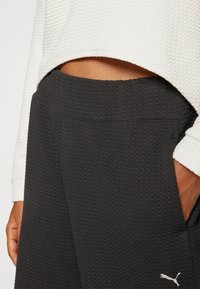 Los joggers negros con textura cuentan con una cinturilla suave y bolsillos laterales, complementados por un logo de la marca en blanco en la parte inferior de la pierna.
