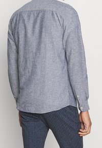 Long-sleeve, button-up shirt made of textured blue fabric with a subtle herringbone pattern, featuring a classic collar and curved hem.