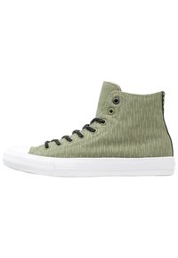 Sneaker alte in tela verde oliva con un motivo testurizzato, lacci neri, suola in gomma bianca e dettagli neri sul retro.