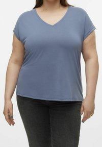 Maglietta a V azzurro chiaro a maniche corte in un tessuto morbido e elastico. Indossata con jeans grigio scuro, presenta una vestibilità rilassata e un design minimalista.