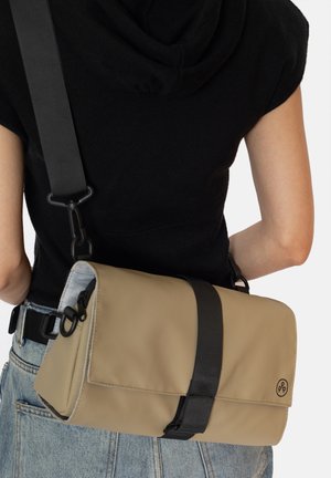 Borsa a spalla rettangolare beige con tracolla nera, dotata di chiusura a patella magnetica e dettaglio con logo. Materiale liscio, design minimalista.