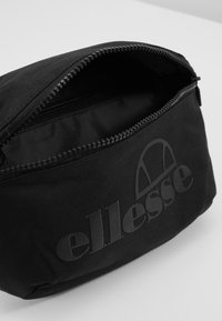 Svart stoffpose med glidelås, med en jevn tekstur og et preget "ellesse"-logo på den ene siden.