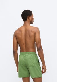 Πράσινα μαγιό σορτς από ελαφρύ ύφασμα, με ελαστική μέση, πλαϊνές τσέπες και πίσω τσέπη με λεπτομέρεια λογότυπου.