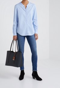 Jasnoniebieska bluzka z długim rękawem w kształcie V, zestawiona z ciemnymi rurkami. Czarna torba tote o fakturowanej powierzchni z brązowymi akcentami oraz botki za kostkę.