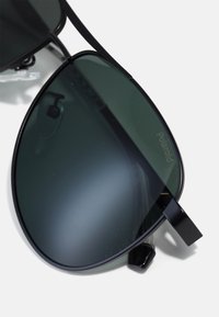 Ochelari de soare aviator negri cu lentile verzi polarizate, având un cadru metalic elegant și un design minimalist. Forma lentilelor este în picătură.