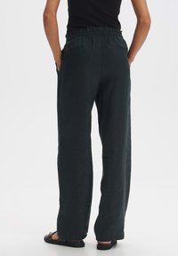 Donker groene linnen broek met een relaxte pasvorm, een elastische tailleband en twee achterzakken. De textuur lijkt zacht met een licht gekreukt uiterlijk.
