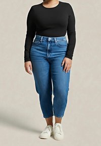 Černý top s dlouhým rukávem spojený s modrými džíny s vysokým pasem. Džíny mají rovný střih a doplňují je bílé tenisky.