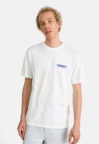 White cotton t-shirt featuring a blue "Carhartt" logo on the left chest area. Short sleeves and a crew neckline, standard fit.