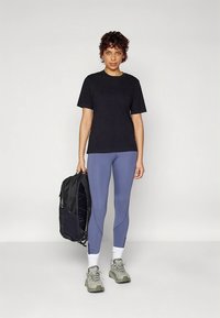 Black short-sleeve t-shirt, blue leggings, gray sneakers, white socks, and a black backpack. Features a simple design and fitted shape.