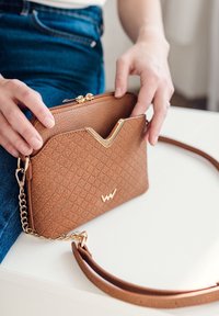 Brown textured handbag with a zip closure and a gold V-shaped accent. Features a detachable strap and a chain link detail.