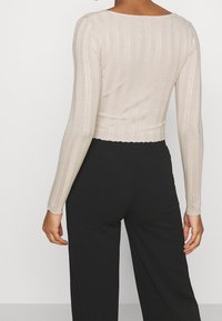 Top court à manches longues beige avec une texture à côtes verticales, col rond et ourlet festonné, associé à un pantalon noir à jambes larges.