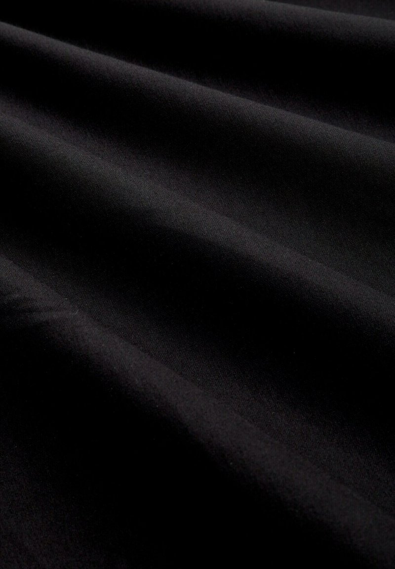 Schwarzer Stoff mit glatter Textur, der subtile Falten und ein mattes Finish aufweist, Licht absorbiert und keine sichtbaren Muster oder Akzente zeigt.