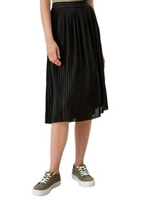 Svart plisserad kjol i lättviktig tyg, med en texturerad midja. Matchad med olivgröna sneakers med vita sulor och snören.