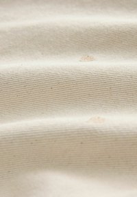 Material din pânză bej deschis cu o textură nervurată, prezentând ușoare neregularități și pete, sugerând o compoziție naturală.